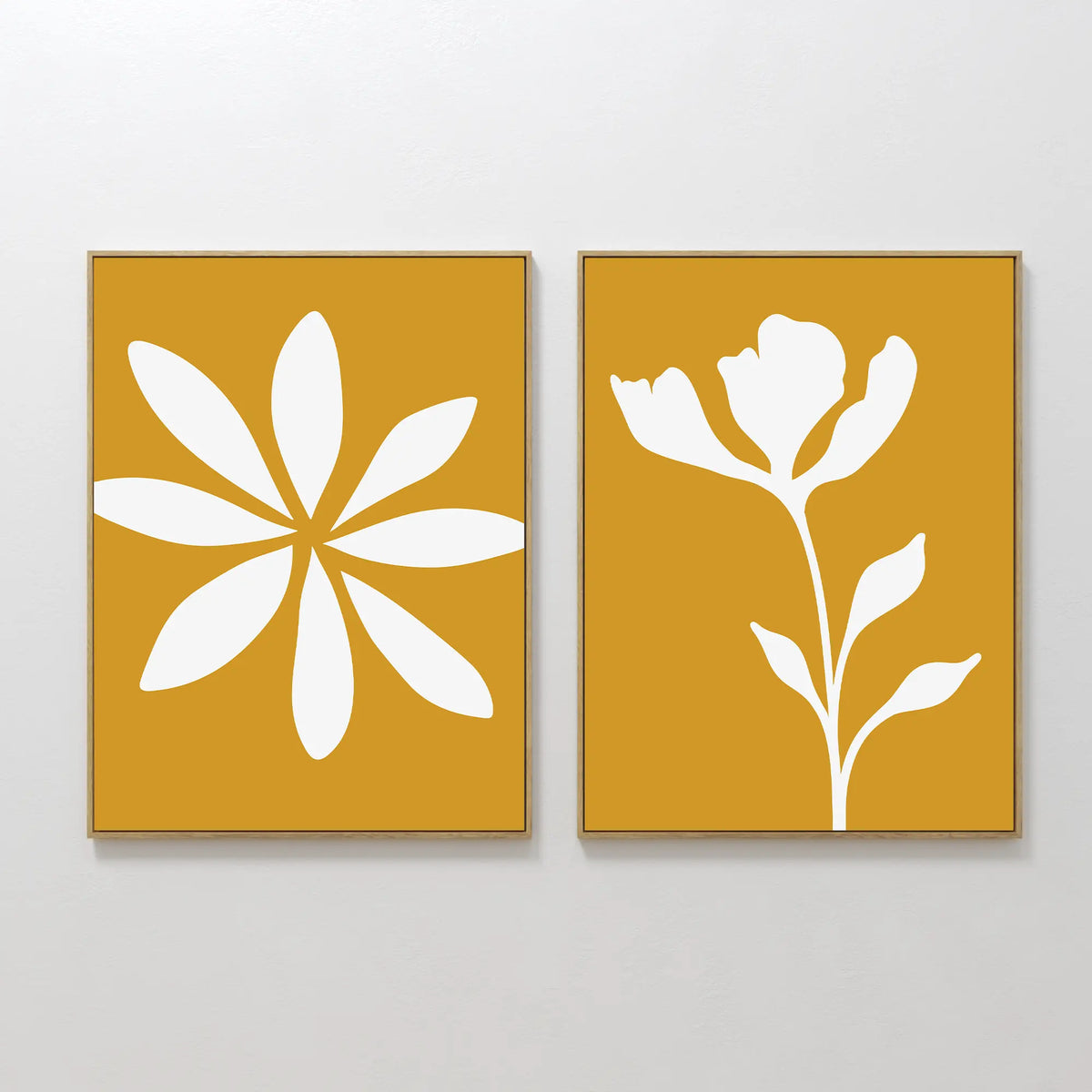 The Golden Bloom Set of 2 features modern wall art: one print with a white abstract eight-petal flower on mustard yellow, and the other with a white silhouette of a blooming flower and leaves—perfect for any space.