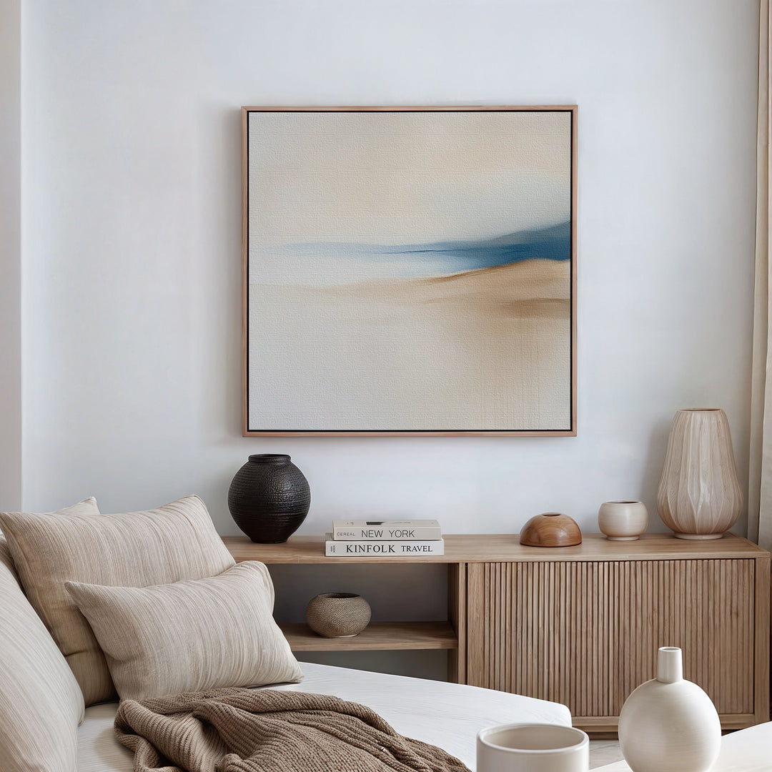 A minimalist living room featuring a cream sofa, neutral pillows, a wooden sideboard with books and vases, and the Golden Drift Canvas Art in calming beige and blue tones—perfect modern decor inspiration.