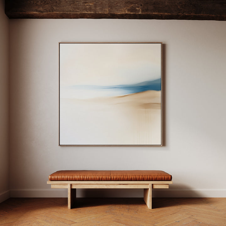 The Golden Drift Canvas Art, with its soft blue and beige abstract design, hangs above a wooden bench with a brown leather cushion. Perfect for living room decor, it complements the wooden floor and exposed ceiling beam.