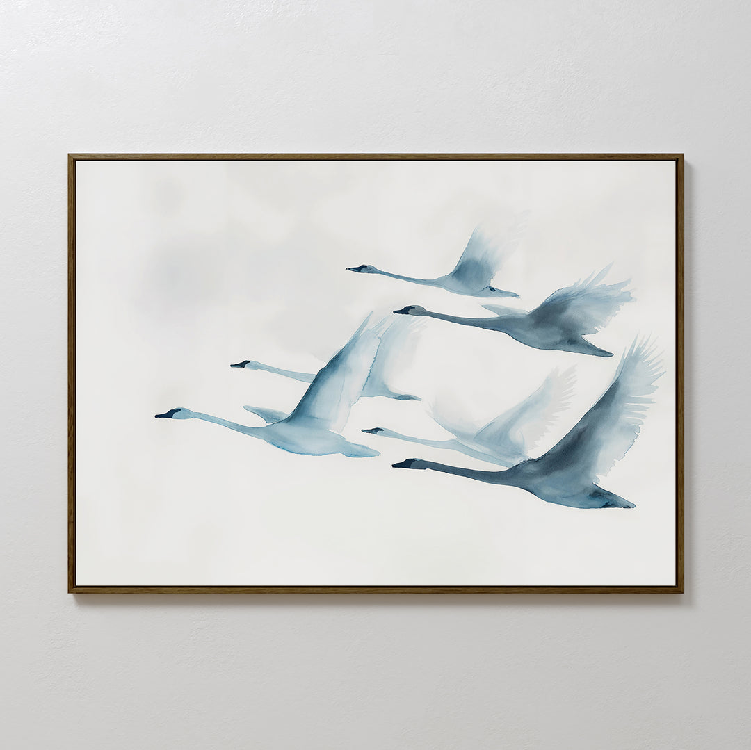 The Graceful Flock Canvas Art showcases six swans in flight, illustrated in soft blue watercolor on a white background, and is framed and displayed on a simple light-colored wall.