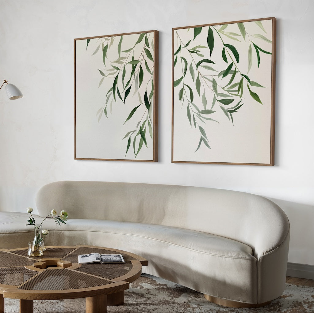 A minimalist living room with a curved light beige sofa, round wooden coffee table, and the Graceful Leaves Set of 2 as elegant framed wall art decor above the sofa.