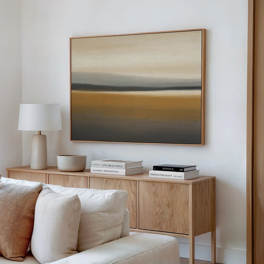 A modern living room features a wooden sideboard with books, a lamp, and bowl. Above it hangs the Honey Mesa Canvas Art in earthy tones. A light-colored sofa is partially visible in this contemporary decor setting.