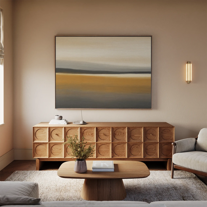 A modern living room with neutral tones features a wooden sideboard, a minimalist coffee table, a light-colored sofa, and the Honey Mesa Canvas Art as minimalist wall art above the seating area.