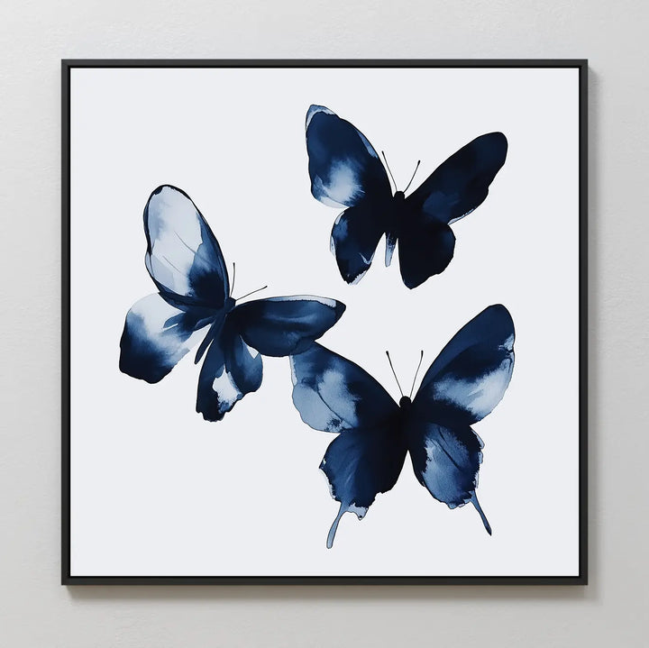 Indigo Flutter Canvas Art showcases three abstract blue watercolor butterflies with soft edges on a white background, set in a simple black frame—ideal for modern home decor.