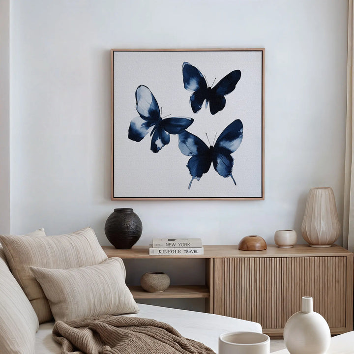 A modern living room with a neutral sofa, wooden sideboard, decorative vases, and the Indigo Flutter Canvas Art featuring three abstract butterflies—an elegant choice for stylish, contemporary home decor.