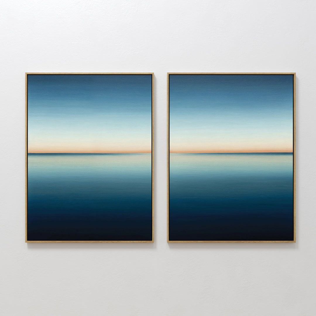 The Indigo Passage Set of 2 features minimalist wall art with framed paintings showing serene seascapes—calm blue water, a gentle horizon, and gradient skies fading from light to deep blue with a soft orange band.
