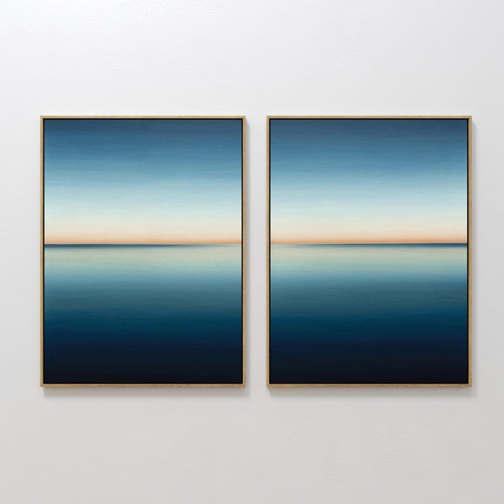 The Indigo Passage Set of 2 features minimalist wall art with framed paintings showing serene seascapes—calm blue water, a gentle horizon, and gradient skies fading from light to deep blue with a soft orange band.