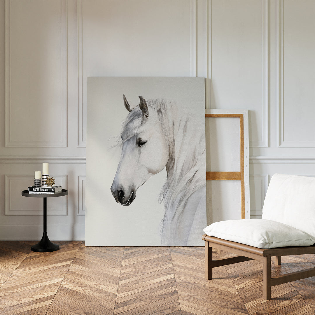 A minimalist room with white paneled walls, wood herringbone floor, a cushioned chair, a small round table with candles and books, and the Ivory Mane Canvas Art—striking white horse print—propped against the wall.
