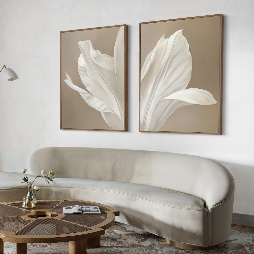 A modern living room with a curved beige sofa, round wooden coffee table, and minimalist wall art—Ivy Petals Set of 2—on a beige wall. A small vase with flowers and an open book add to this stylish living room decor.