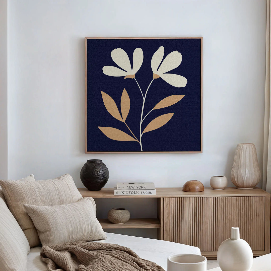 A minimalist living room with a beige sofa, neutral cushions, and modern decor. The Ivory Stems Canvas Art, featuring ivory stems and white and tan flowers on a dark background, hangs above the wooden sideboard.