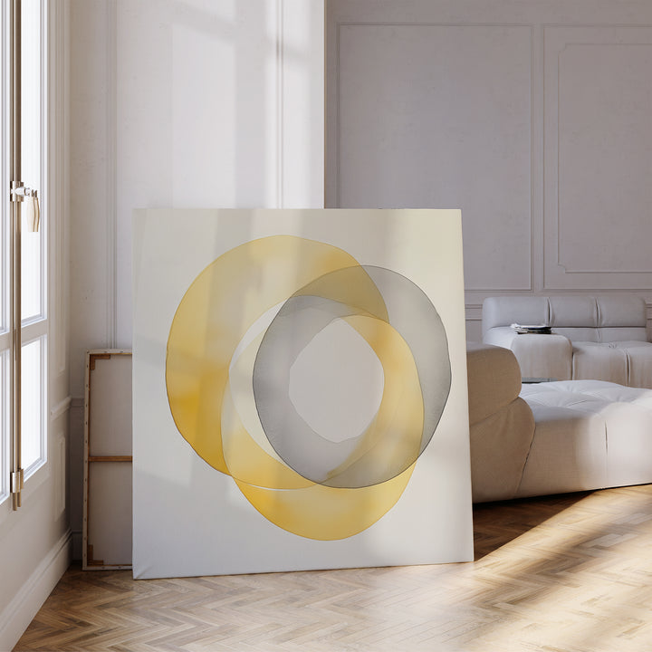 A sunlit modern living room features the Lemon Light Canvas Art—an abstract print with overlapping yellow and gray circles—propped against the wall near a white sofa and large window.