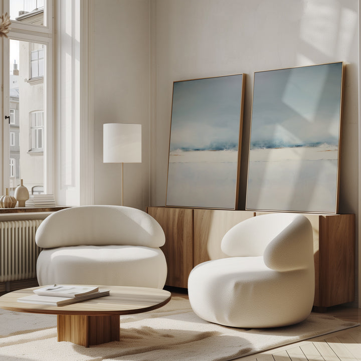 A modern living room features the Misty Morning Set of 2 rounded white armchairs, a low wooden coffee table, and a wooden sideboard with minimalist Nordic Park wall art. Sunlight from a tall window creates a tranquil atmosphere.