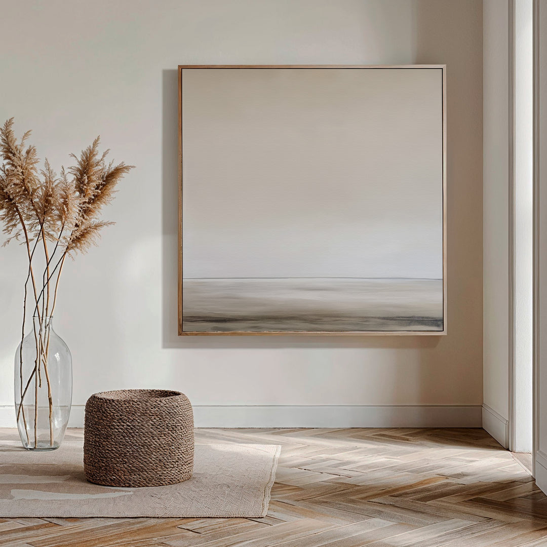 Minimalist living room featuring the Morning Mist Abstract Canvas Art as serene wall décor, a clear vase with dried pampas grass, a woven basket, and light wood herringbone flooring bathed in natural sunlight.