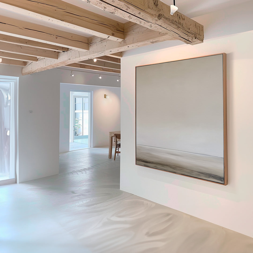 A minimal, modern room with light wooden beams and white walls is accented by the Morning Mist Abstract Canvas Art in neutral tones, adding elegance as natural light streams through windows and highlights smooth floors.