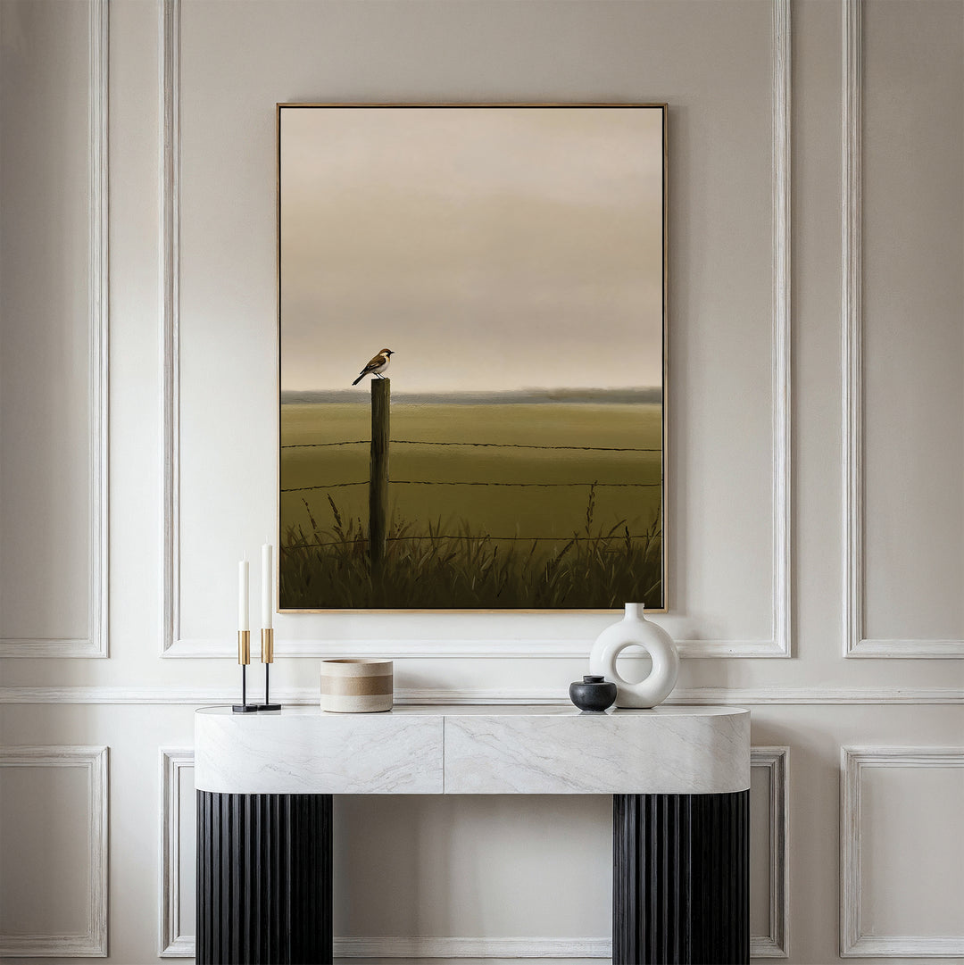 A minimalist room features a marble console with decor, topped by the Morning Perch Canvas Art—a bird on a fence post in a misty green field—adding subtle charm to earthy interiors.