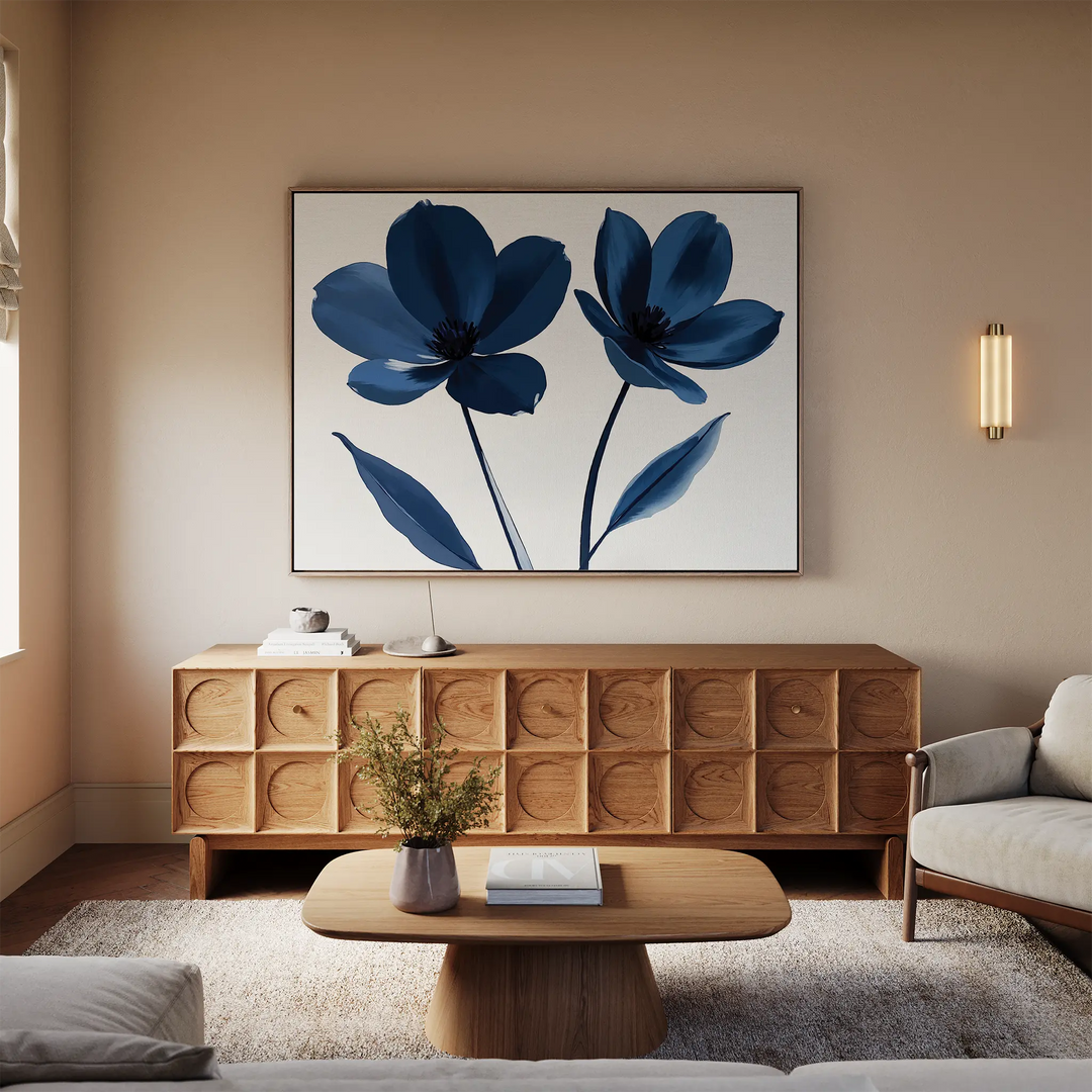 A modern living room with neutral sofas, a wooden sideboard, coffee table, and a bold Navy Flora Canvas Art featuring two blue flowers as large wall decor above the sideboard. A small plant accents the coffee table.