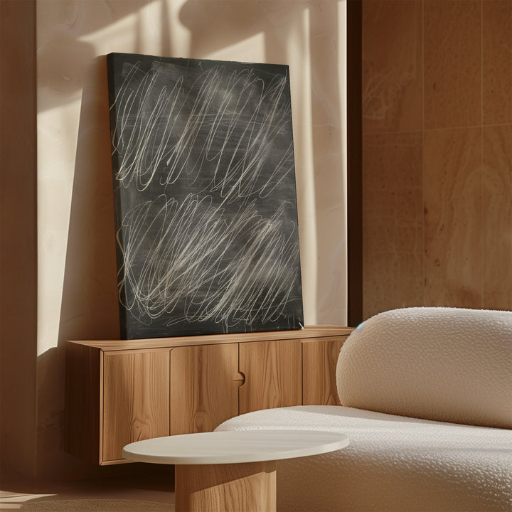 The Echoes in Chalk Abstract Canvas Art, featuring minimalist white markings on black, leans against a beige wall atop a wooden cabinet beside a textured white sofa and round coffee table in a sunlit room.