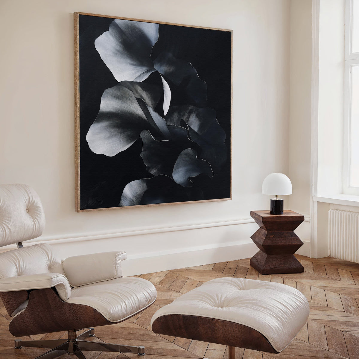 A modern living space highlights Nocturnal Bloom Abstract Canvas Art—a black-and-white floral painting—paired with a cream leather lounge chair, ottoman, geometric wooden side table, and white lamp by a tall window.