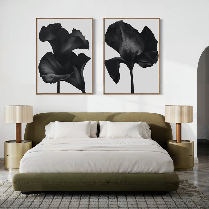 A modern bedroom featuring a green upholstered bed with white bedding, two beige bedside tables and matching lamps, and the Noir Bloom Set of 2 black floral prints displayed above the bed.
