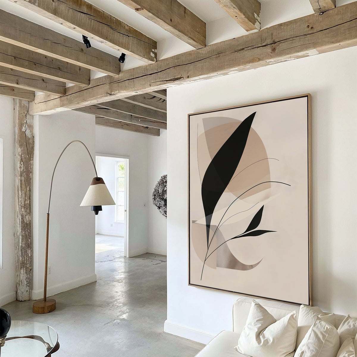 A bright, modern living space with wooden ceiling beams, a beige arc floor lamp, and white couch. The Noir Petals in Motion Abstract Canvas Art with black and beige shapes accents the white wall in this stunning design.