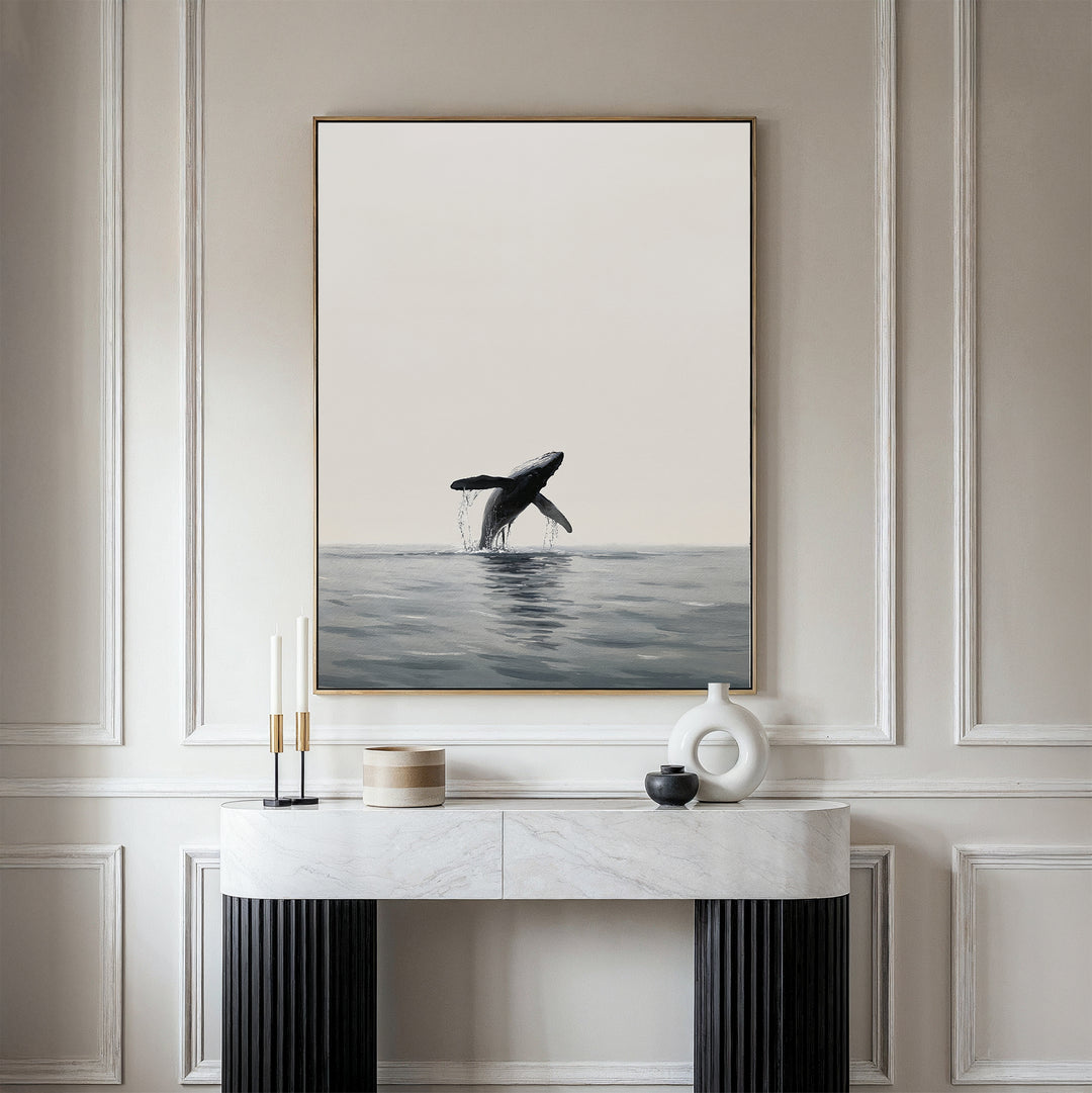 A minimalist room with a marble console table, decorative objects, and Ocean Leap Canvas Art—a large framed painting of a breaching whale—hanging on a light-colored paneled wall.