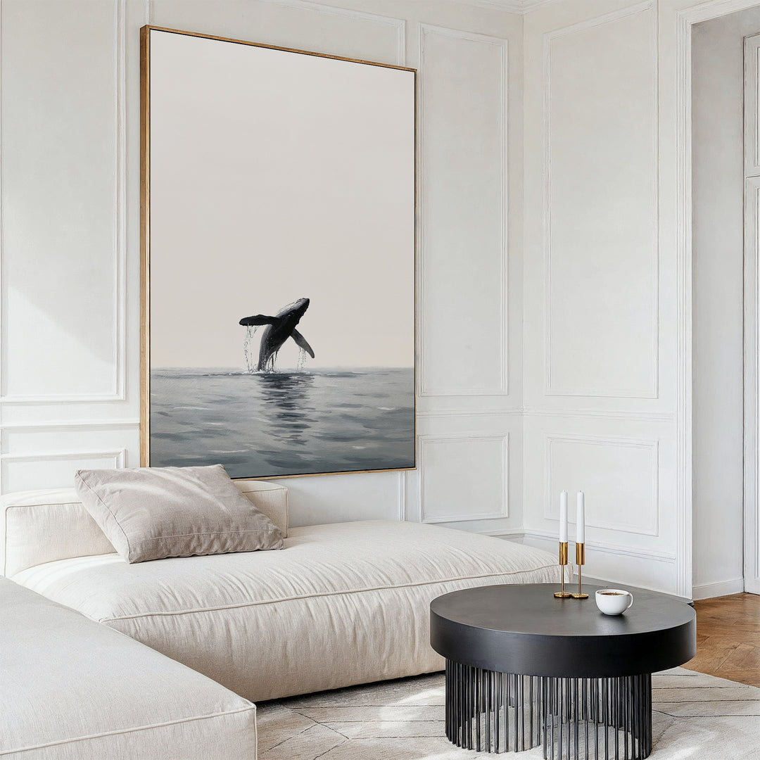 A modern living room with a cream sofa, round black coffee table, two candlesticks, and the striking Ocean Leap Canvas Art—a large framed painting of a breaching whale—hanging on a white paneled wall.