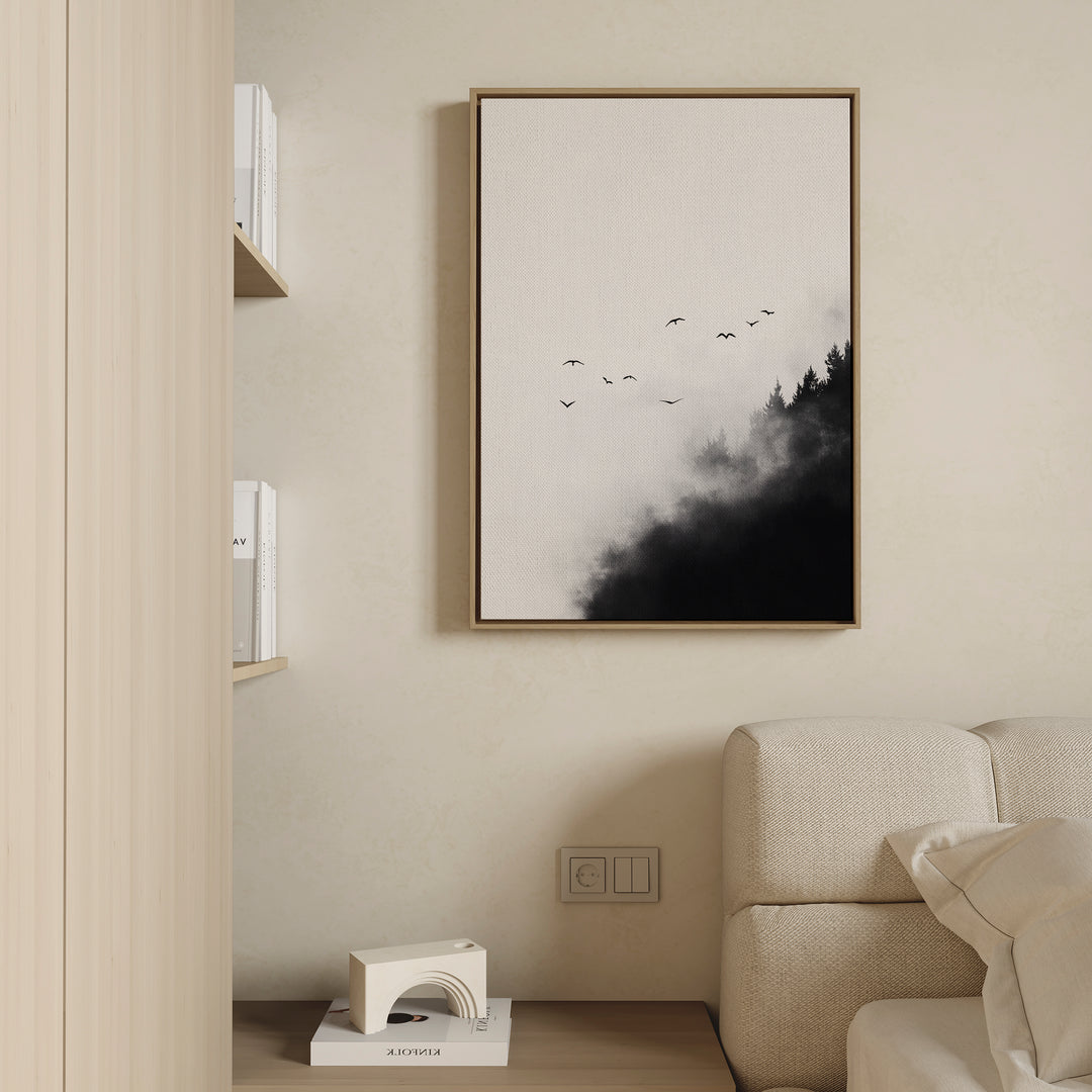 A minimalist living room features a light sofa, bookshelf, and Passing Pines Canvas Art with birds soaring above misty trees. Large wall art and a neutral color palette enhance the modern aesthetic.