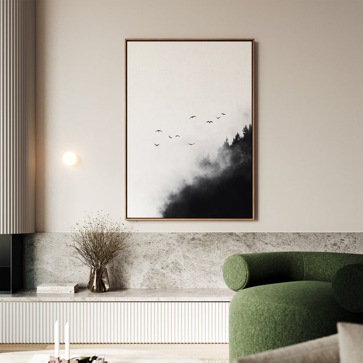 A modern living room features a green curved sofa, wall-mounted light, and large Passing Pines Canvas Art showing birds over misty trees. Below, a low table holds candles and a vase of dried branches.