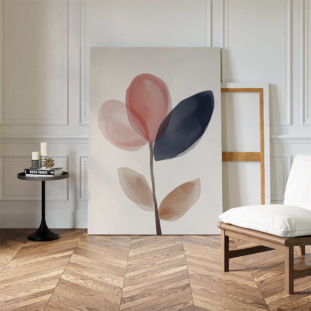 A modern room with herringbone wood floors features the Petal Breeze Canvas Art—abstract watercolor leaves in muted red, blue, and beige—propped by a chair and black side table with candles and books. Ideal for living room decor.