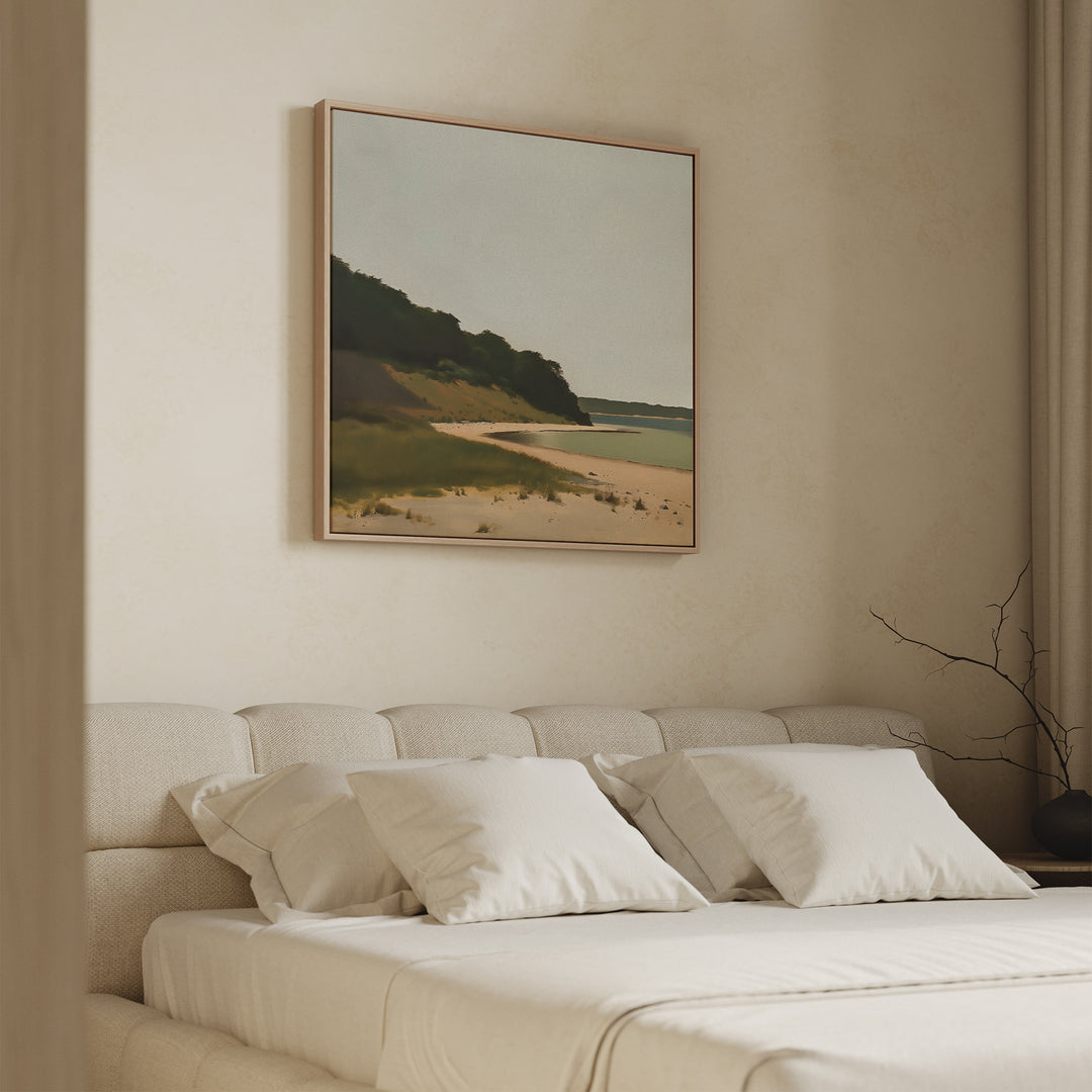 A cozy, minimal bedroom features a beige bed, white pillows, and Quiet Bend Canvas Art—a serene landscape with beach and greenery—above the headboard. Neutral walls and simple decor complete the calm, tranquil vibe.