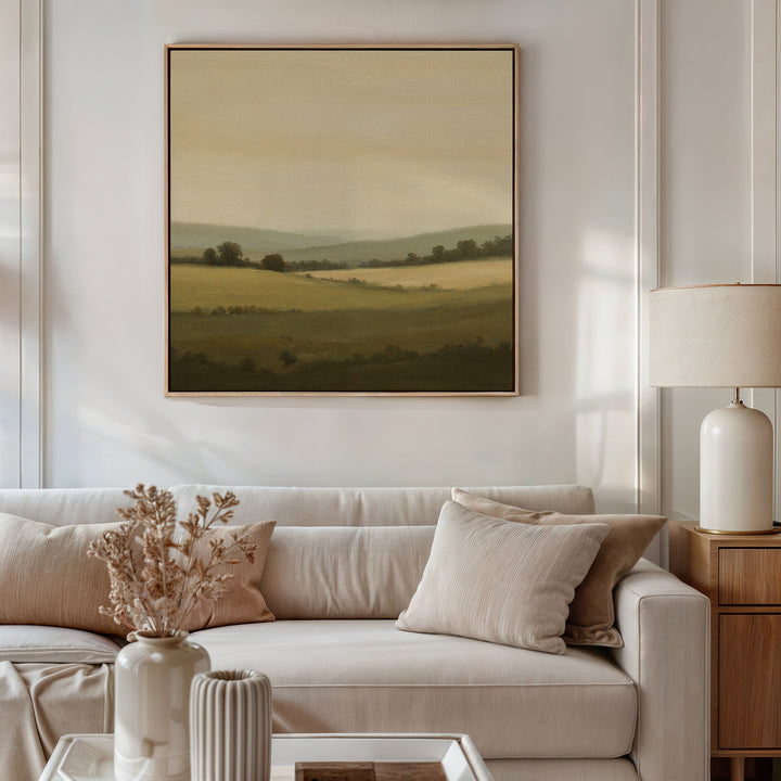 A neutral living room with a beige sofa, cream pillows, table lamp, dried flowers in a vase, and minimalist Quiet Countryside Canvas Art of rolling hills displayed above the couch.