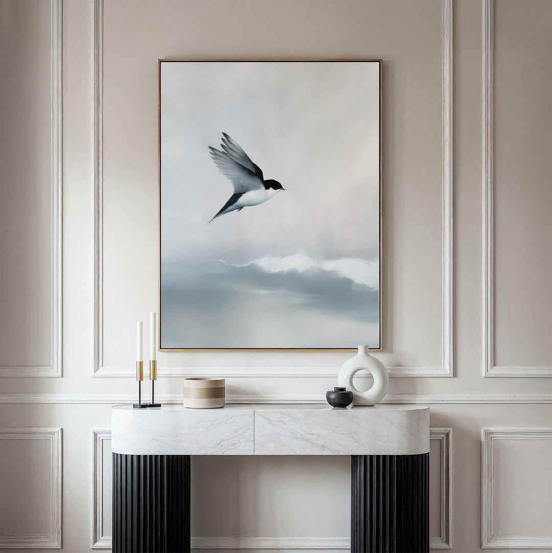 A minimalist console table sits against a beige paneled wall, topped by the Quiet Flight Canvas Art featuring a bird in flight over misty clouds, adding elegance and Nordic Park-inspired charm to the space.
