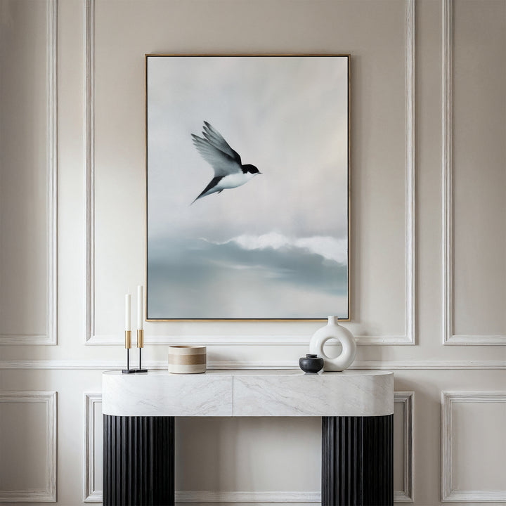 A minimalist console table sits against a beige paneled wall, topped by the Quiet Flight Canvas Art featuring a bird in flight over misty clouds, adding elegance and Nordic Park-inspired charm to the space.