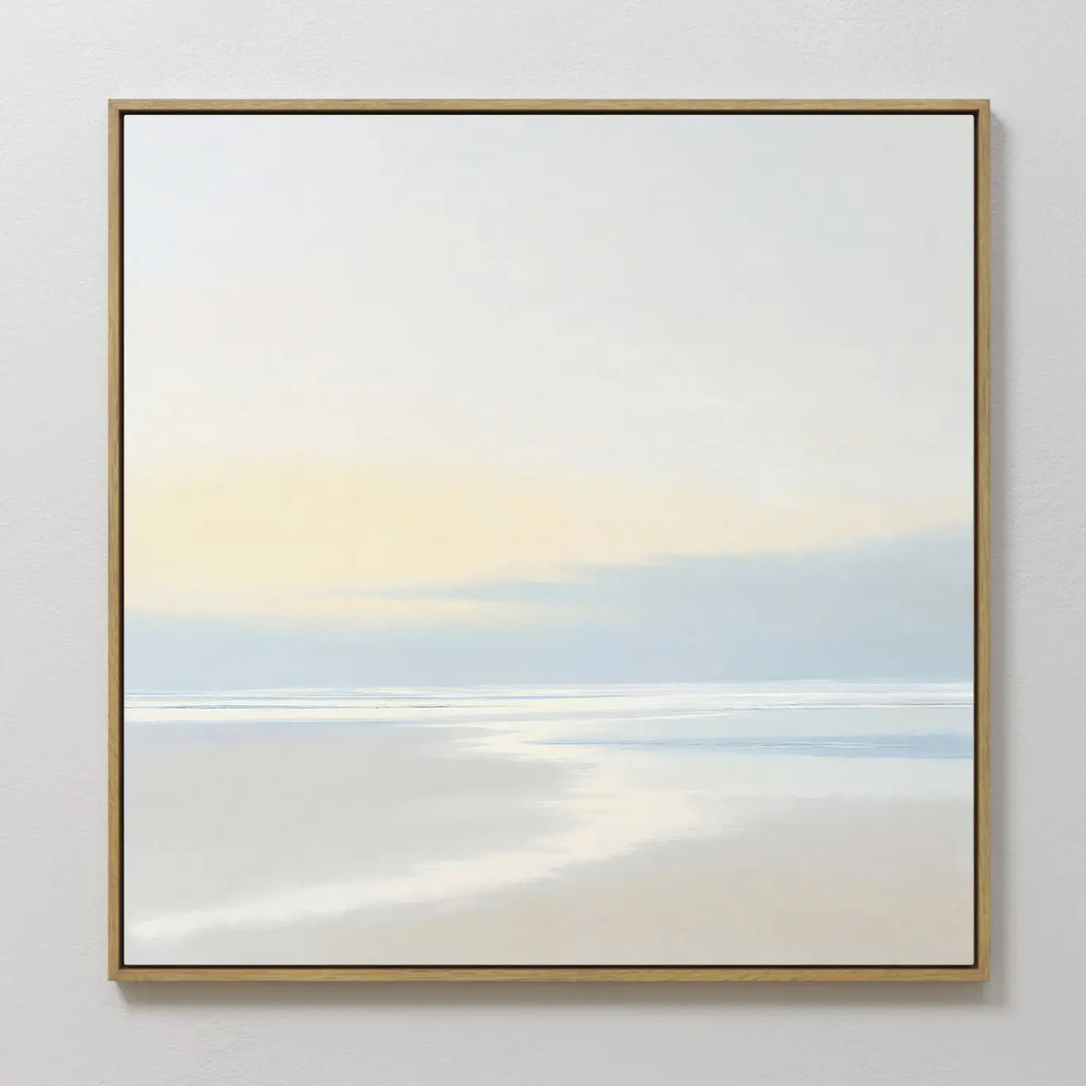 Quiet Shores Canvas Art features a minimalist seascape with soft pastels, a pale sky, and gentle clouds. Framed in thin gold and displayed on a white wall, its perfect coastal decor for any space.