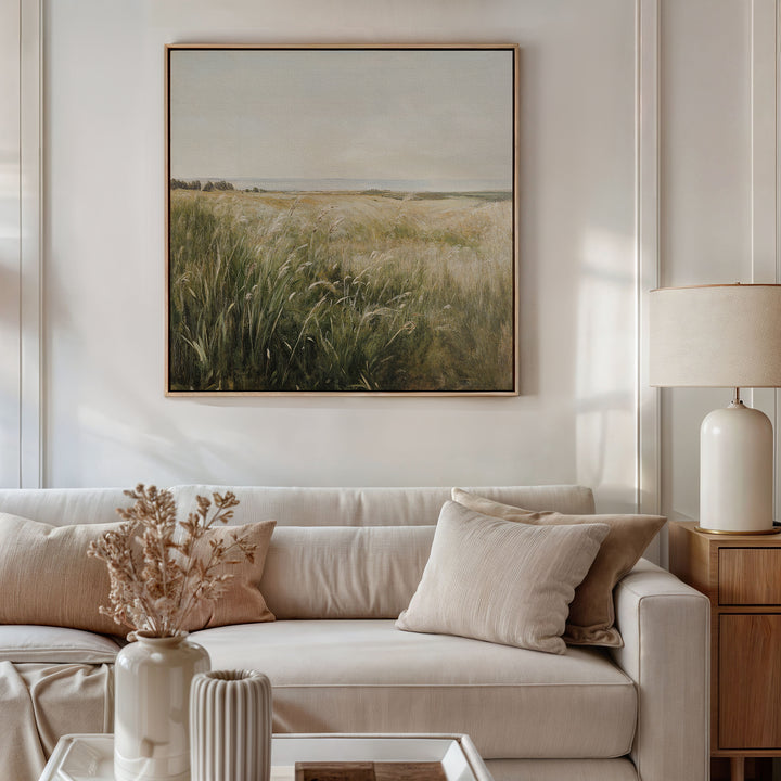 A neutral-toned living room features a white sofa, beige pillows, and vases on a side table. Above the sofa hangs the Reeds by the River Canvas Art, adding serene decor and completing this tranquil space.