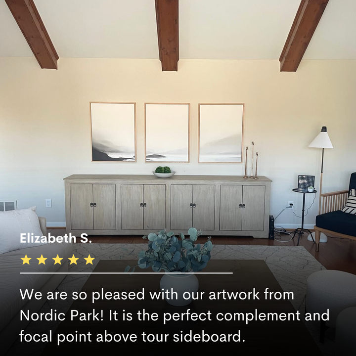 A light wood sideboard sits against a cream wall, topped with minimal decor. Above, the Serenity Peaks Set of 3 abstract landscape prints are evenly spaced. Exposed wooden beams and neutral modern furnishings create a serene balance.