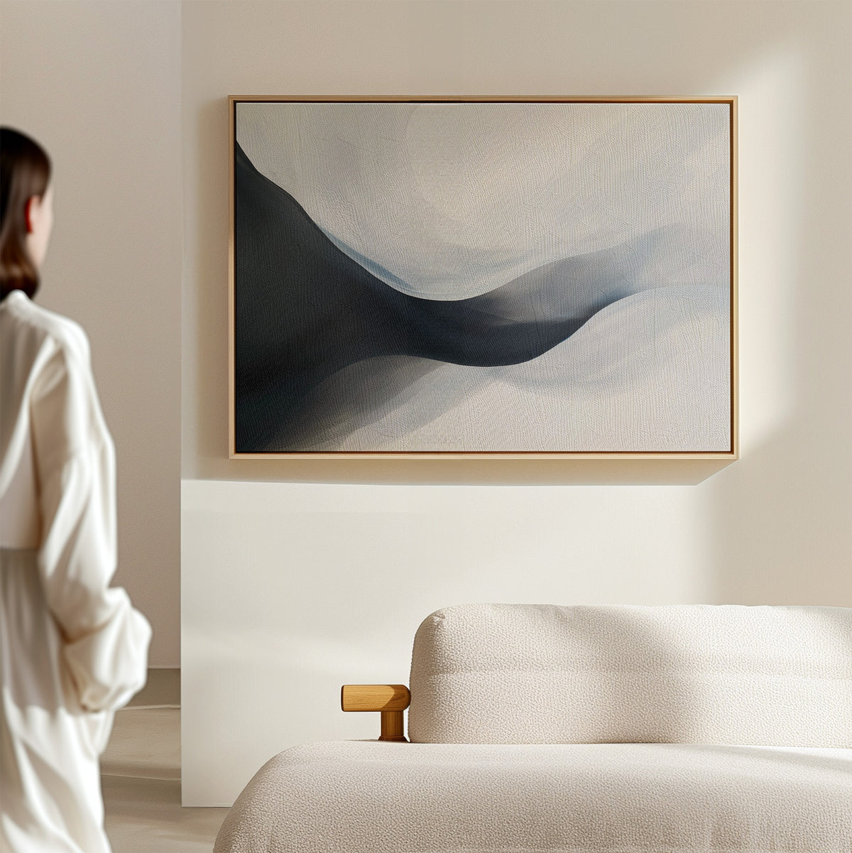 A person stands in a sunlit, minimal room with a beige sofa, admiring the Rippling Vista Abstract Canvas Art—a serene wall print with soft blue and gray shapes that perfectly embodies modern elegance.