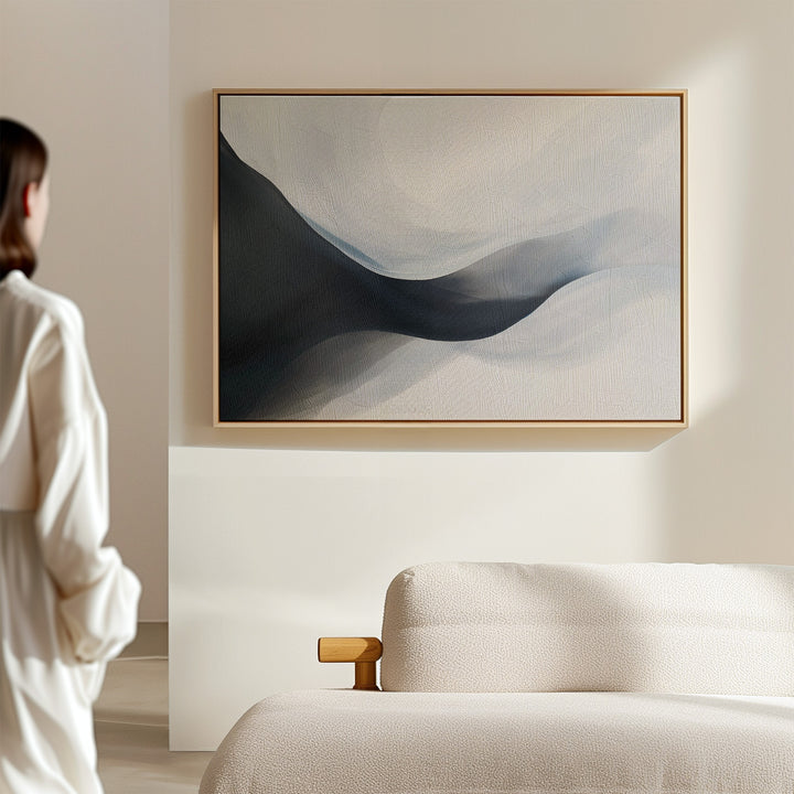 A person stands in a sunlit, minimal room with a beige sofa, admiring the Rippling Vista Abstract Canvas Art—a serene wall print with soft blue and gray shapes that perfectly embodies modern elegance.