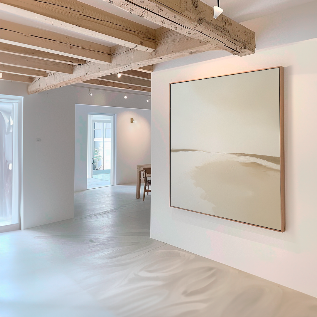 A minimalist room with white walls and light wooden beams features the Serene Expanse Abstract Canvas Art by My Store in neutral tones, while sunlight streams through windows and a dining area complements the modern living room decor.