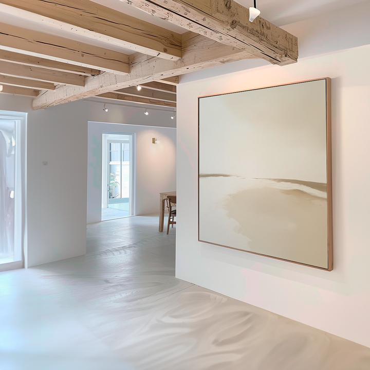 A minimalist room with white walls and light wooden beams features the Serene Expanse Abstract Canvas Art by My Store in neutral tones, while sunlight streams through windows and a dining area complements the modern living room decor.