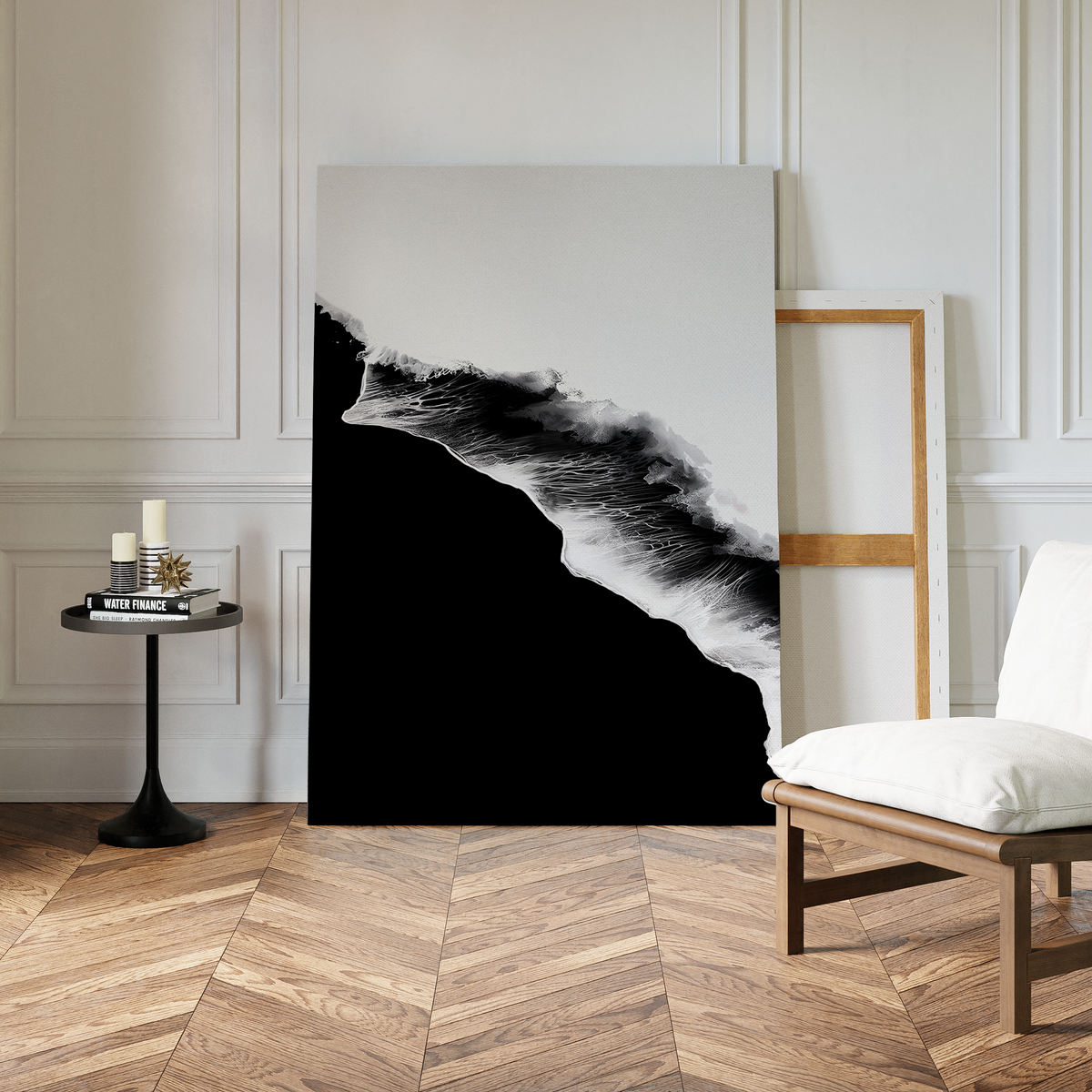 A modern room with chevron wood flooring features the Black Ocean Abstract Canvas Art propped against a wall in a wooden frame, alongside a white cushioned chair and a small black table with candles and books.