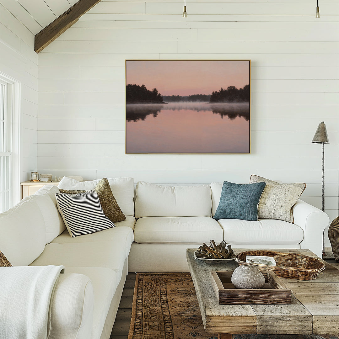 A cozy living room with a white sectional, neutral and blue pillows, a rustic coffee table, and Rose Lake Canvas Art—a large landscape lake scene at sunset—framed on a white shiplap wall.