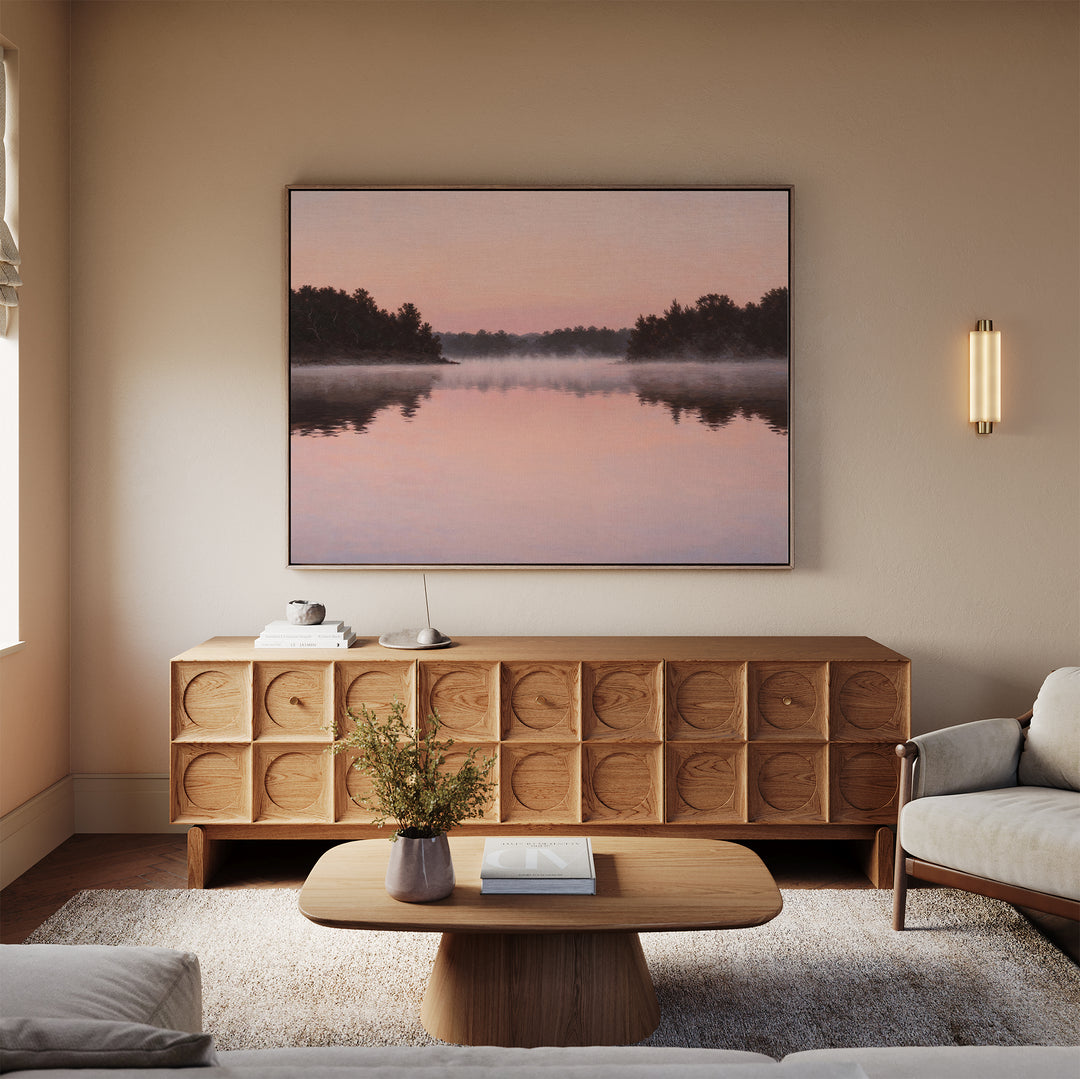 A cozy living room with beige walls, a light wood coffee table, matching sideboard, light sofa, and Rose Lake Canvas Art—a large framed landscape painting of a misty pink lake—above the sideboard.