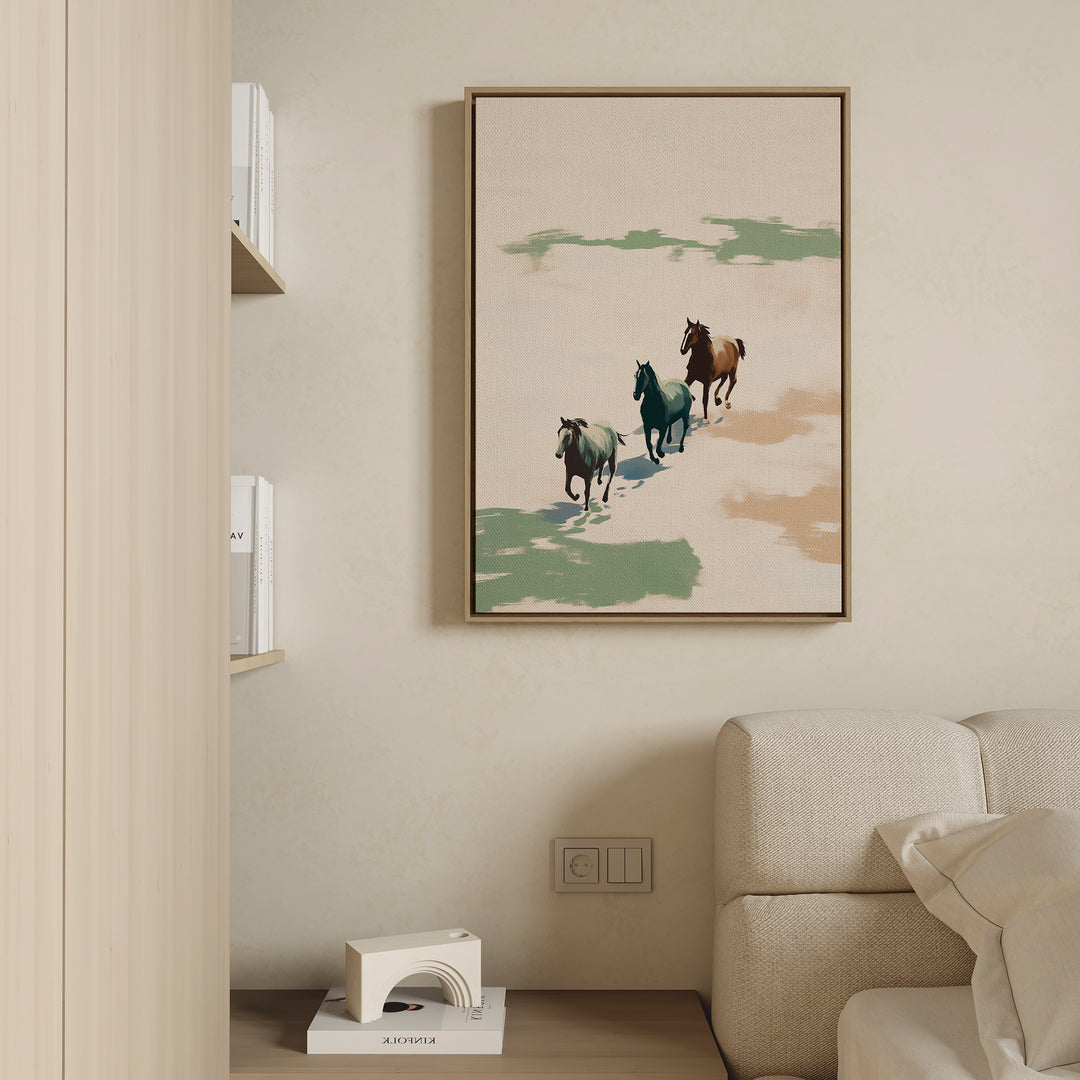 The Running Free Canvas Art, featuring three horses running, hangs above a light couch on a beige wall in this modern minimal living room. A portion of a bookshelf and a small decorative item complete the scene.