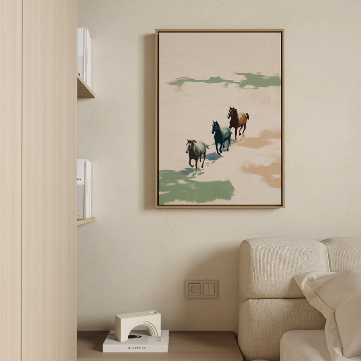 The Running Free Canvas Art, featuring three horses running, hangs above a light couch on a beige wall in this modern minimal living room. A portion of a bookshelf and a small decorative item complete the scene.