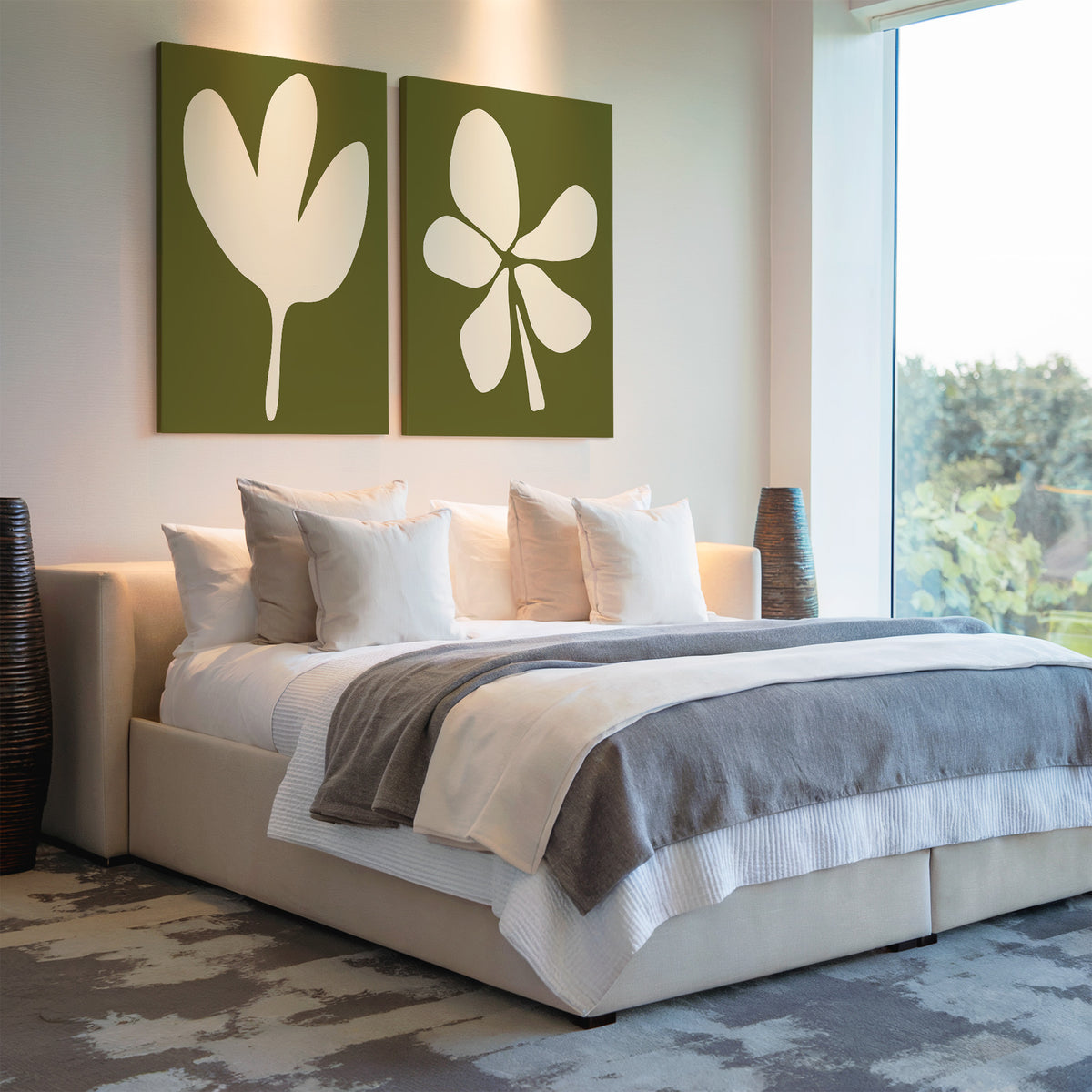 A modern bedroom with a large bed, white and gray bedding, sage green accents, the Sage Petal Set of 2 abstract leaf wall art above the headboard, woven vases on each side, and a large window letting in natural light.