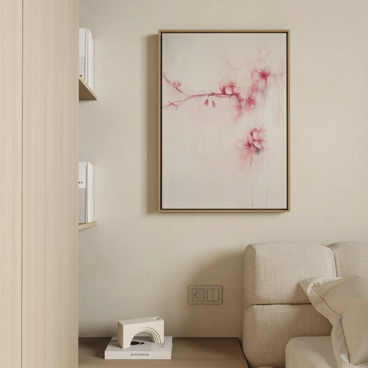 A minimalist living room corner features a light beige sofa, a small bookshelf, and the Sakura Dream Canvas Art, which displays delicate pink flowers on a white background. Neutral tones throughout create a calm, inviting atmosphere.