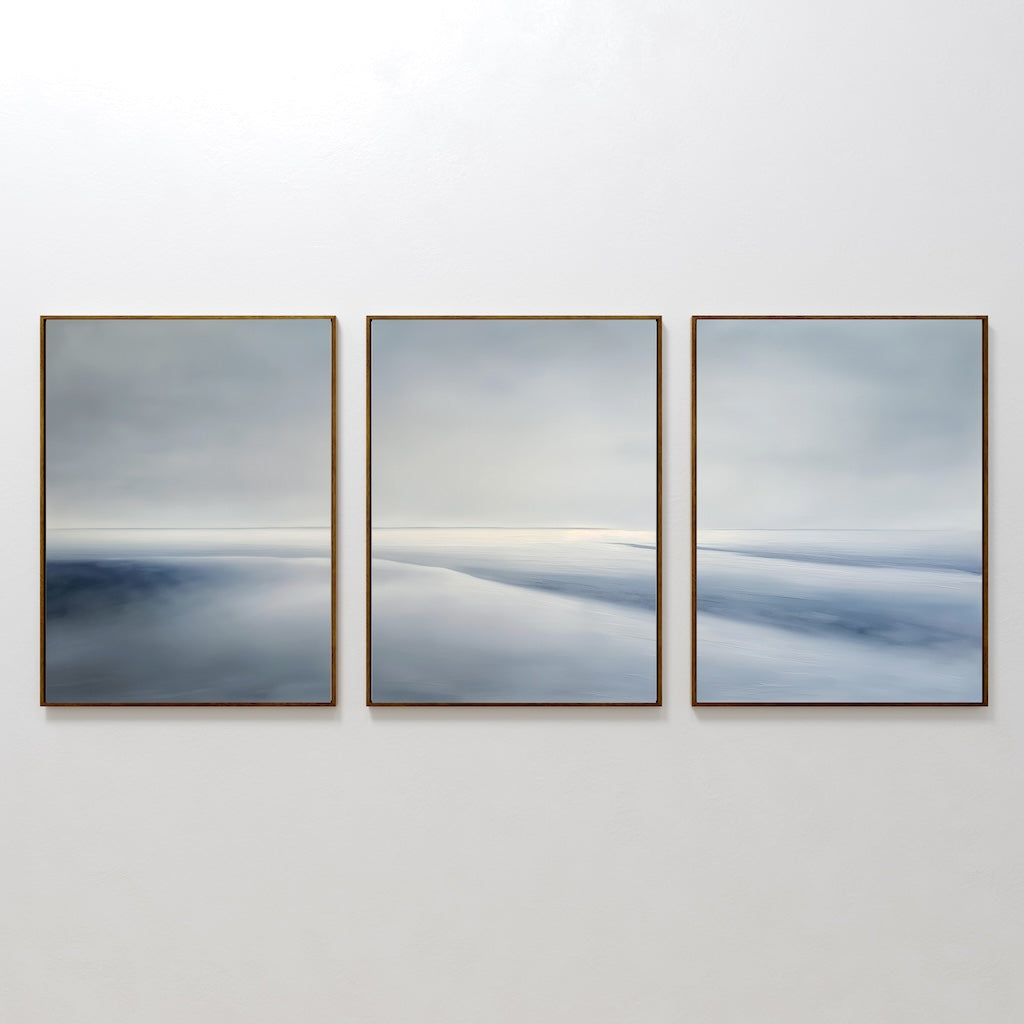 The Serene Horizons Set of 3 features framed abstract wall art prints with soft, blurred shades of blue, gray, and white—arranged side by side to create a calming, minimalist landscape on any wall.