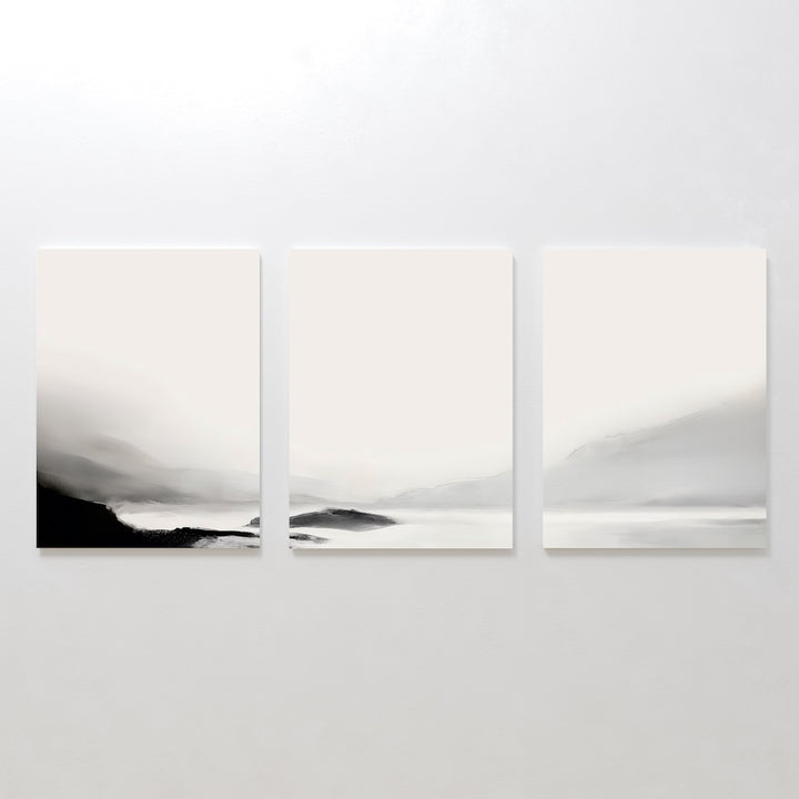 The Serenity Peaks Set of 3 features minimalist, monochrome landscape paintings with soft black, gray, and white gradients depicting foggy mountains and tranquil water in a modern style, perfect for a serene wall display.
