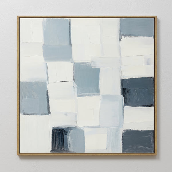 Silent Squares Abstract Canvas Art showcases overlapping rectangular blocks in white, cream, and blue-gray, framed in a slim gold frame. This minimalist piece is perfect for modern home decor displayed against a white wall.